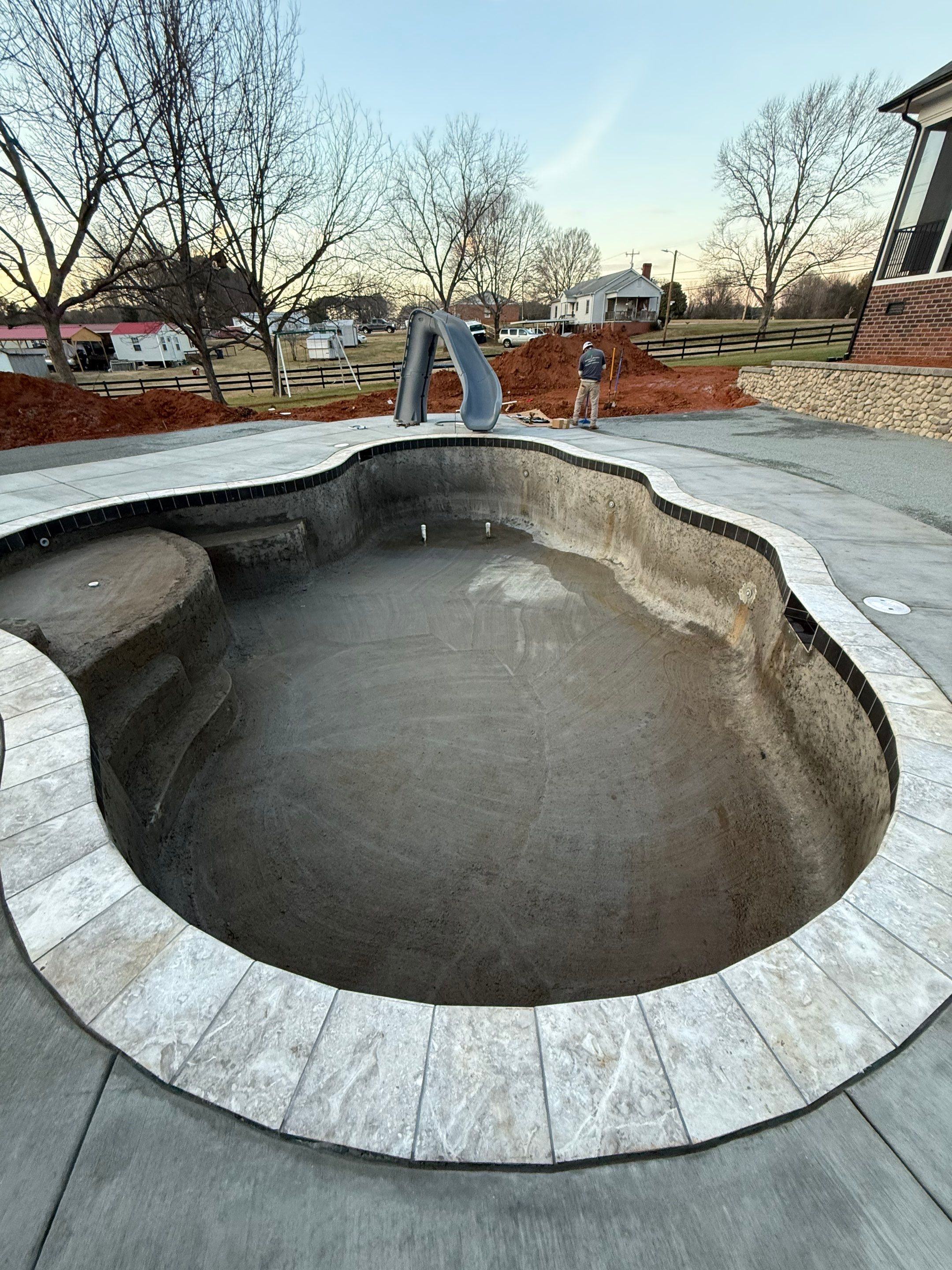Freeform concrete pool shell with travertine coping and slide under construction